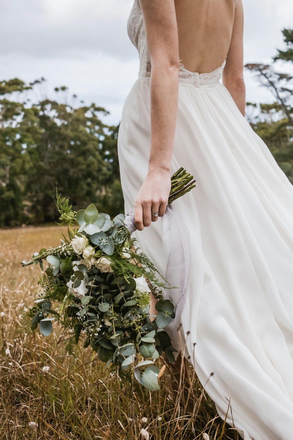 Frau im weißen Brautkleid mit Blumenstrauß in der Hand