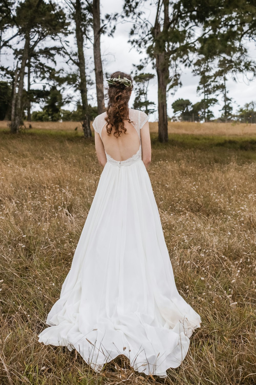 Mujer con vestido de novia sin espalda de pie en medio del campo de hierba marrón