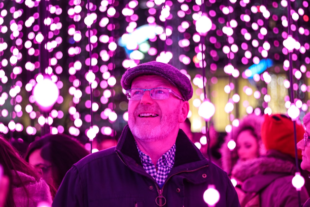 man in black jacket looking at the purple string lights