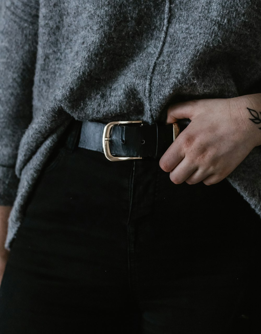 person wearing black and silver belt with buckle, black bottoms, and gray top