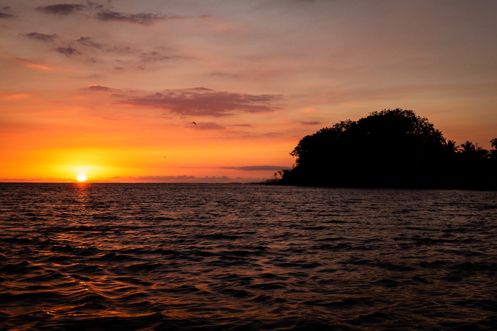 silhouette of island with calm sea during sunset