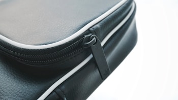 A close-up view of a black leather bag with a visible zipper. The bag features a white trim line, adding contrast against the black surface. The texture of the leather and the design of the zipper are clearly visible.