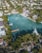 An aerial view of an upscale residential area featuring a large, serene body of water surrounded by lush greenery and palm trees. Elegant houses with swimming pools line the water's edge, some with private docks extending into the water. Several boats are moored nearby, and the area is densely populated with trees and vegetation.