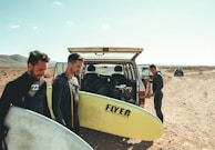 man wearing black wetsuit holding white surfboard surf trip 