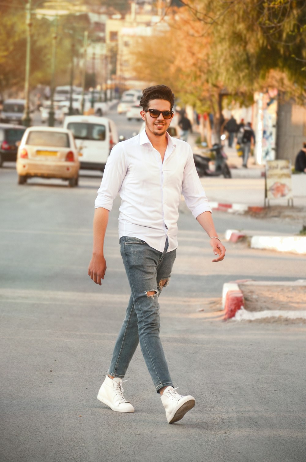 hombre con camisa de vestir blanca y jeans azules desgastados de pie en la carretera