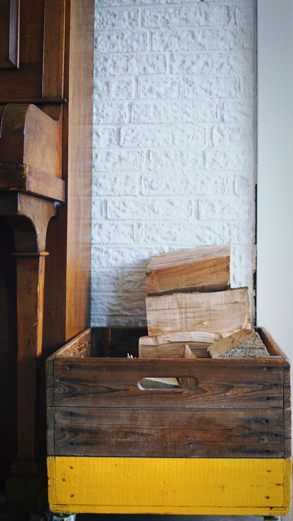 a wooden box filled with wood next to a white brick wall