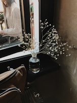 Hands arranging fresh flowers in a simple white moose ceramic vase on a sunlit windowsill.