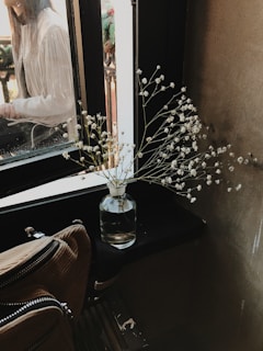 Hands arranging fresh flowers in a simple white moose ceramic vase on a sunlit windowsill.