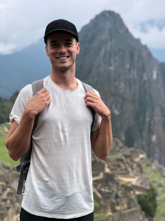 smiling man in white crew-neck t-shirt with black fitted cap holding backpack in Camino Inca Peru