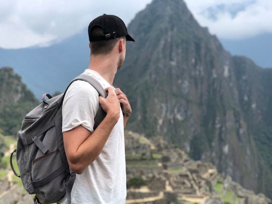 man wearing white shirt with backpack facing green mountain in Machu Picchu Peru