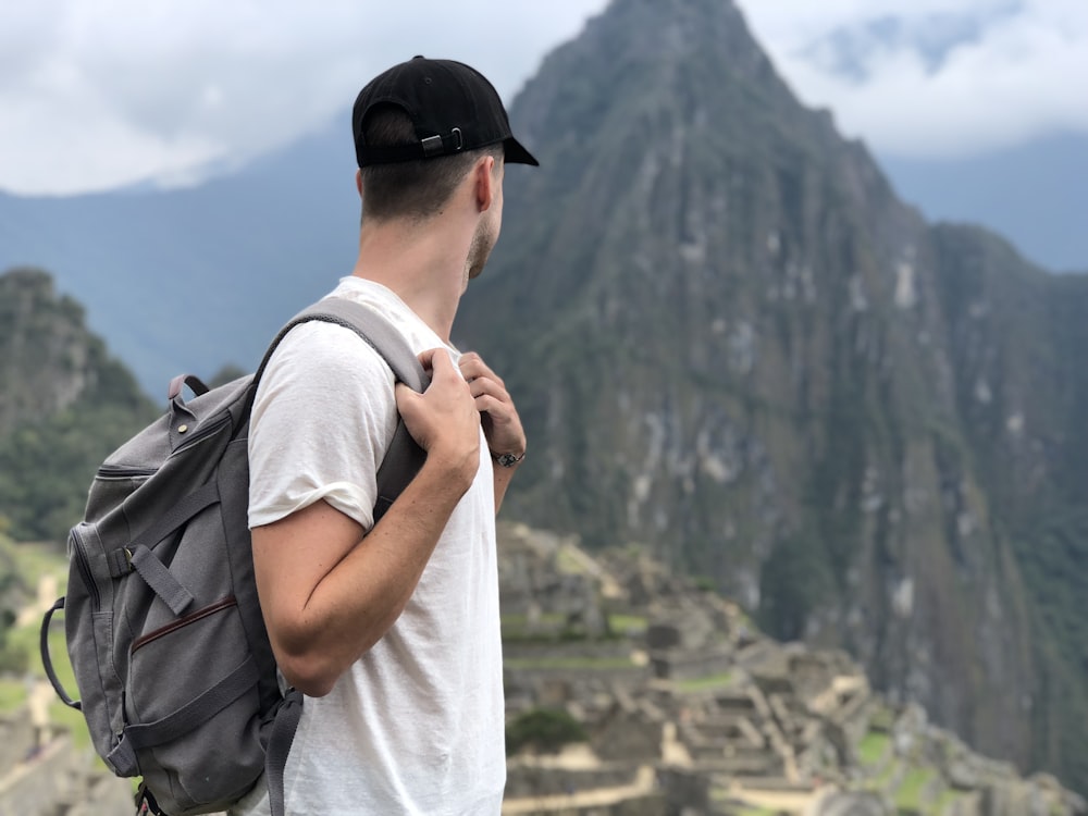 man wearing white shirt with backpack facing green mountain