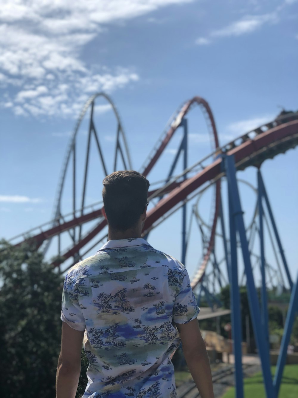 man in white greenn floral shirt standing facing the roller coaster