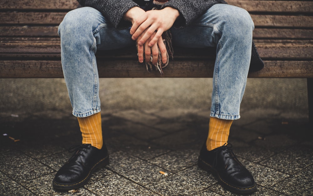 person in blue denim jeans sitting on brown bench