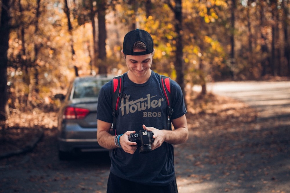 smiling man standing near vehicle holding camera during daytime