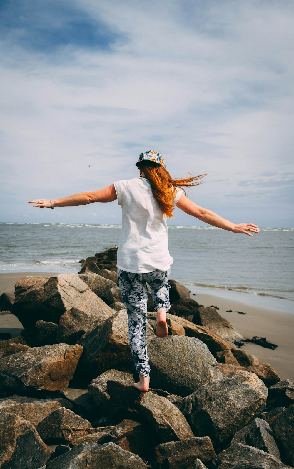 man wearing white 5-shirt stepping on rocks near sea