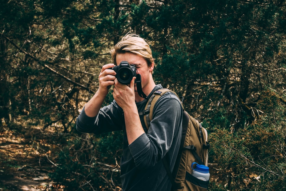 man in sweater carrying brown backpack and holds black DSLR camera