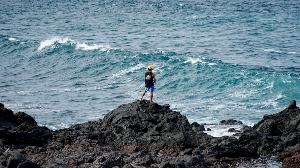 man in black tank top stands on top of rocks in beach