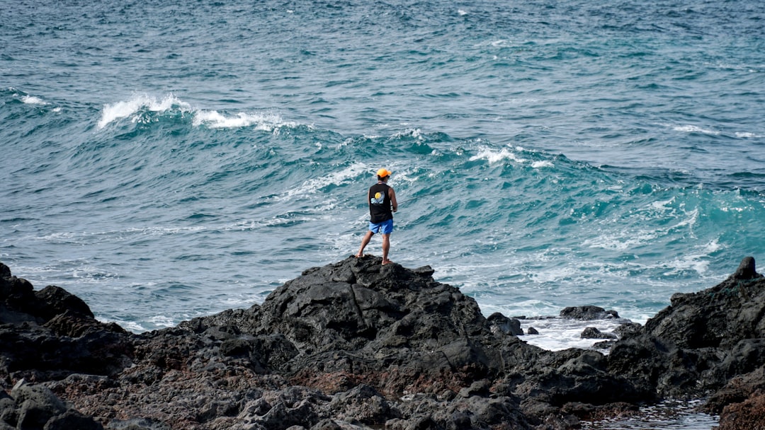 man in black tank top stands on top of rocks in beach,