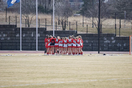 group of girls in white-and-red top hugging on field during daytime