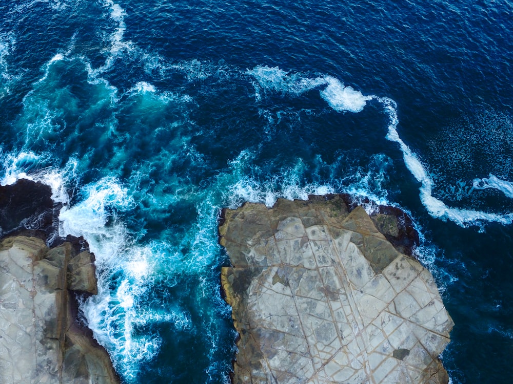 fotografia aérea de ondas do mar atingindo rochas costeiras durante o dia