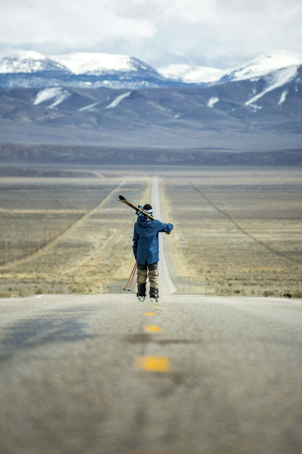 person standing on the middle of road facing snowy mountain