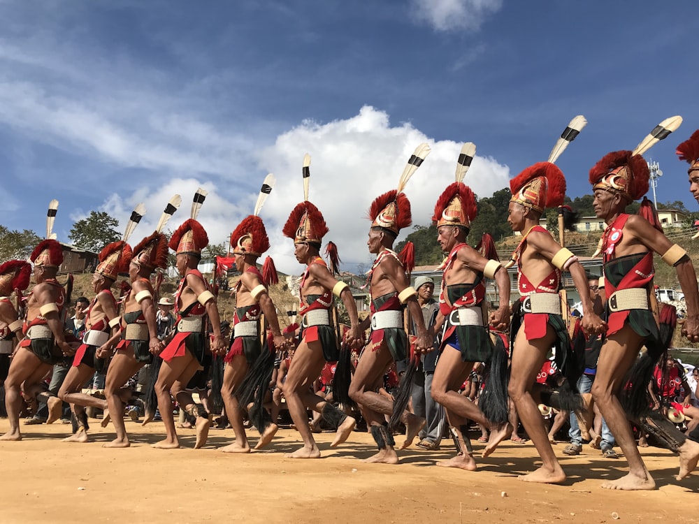 men on red and black traditional costumes dancing on dirt ground barefooted