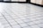 A close-up view of a grid pattern formed by a series of small, shiny white ceramic tiles. The surface appears clean and polished, with light reflecting softly off the tiles, creating a slightly glossy effect. The background is blurred, which emphasizes the uniform arrangement and texture of the tiles.