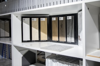 Several wood samples displayed on a white shelf, each with a different wood color and texture. Surrounding these samples are various design catalogs and color swatches.