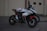 A sports motorcycle is parked on a paved surface with a textured background. The bike features a sleek design with prominent branding and a combination of black, red, and white colors. On top of the motorcycle seat, a helmet with a stylized design is placed.