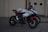 A sports motorcycle is parked on a paved surface with a textured background. The bike features a sleek design with prominent branding and a combination of black, red, and white colors. On top of the motorcycle seat, a helmet with a stylized design is placed.