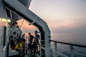 A group of sailors sharing a warm meal together on a ship deck at sunset.
