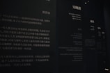 The image features a dimly lit wall with Chinese text printed in white on a dark background. The text appears to be part of an exhibit or informational display, possibly in a museum or gallery. Multiple columns and sections of text are visible, with some larger characters and headings near the top.