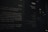 The image features a dimly lit wall with Chinese text printed in white on a dark background. The text appears to be part of an exhibit or informational display, possibly in a museum or gallery. Multiple columns and sections of text are visible, with some larger characters and headings near the top.