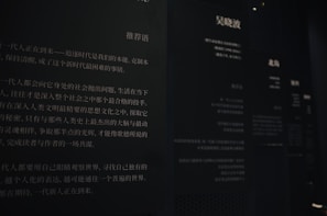 The image features a dimly lit wall with Chinese text printed in white on a dark background. The text appears to be part of an exhibit or informational display, possibly in a museum or gallery. Multiple columns and sections of text are visible, with some larger characters and headings near the top.