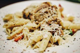 Close-up of a steaming box filled with creamy Alfredo pasta, garnished with fresh parsley.