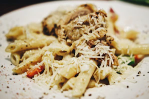 Close-up of a steaming box filled with creamy Alfredo pasta, garnished with fresh parsley.