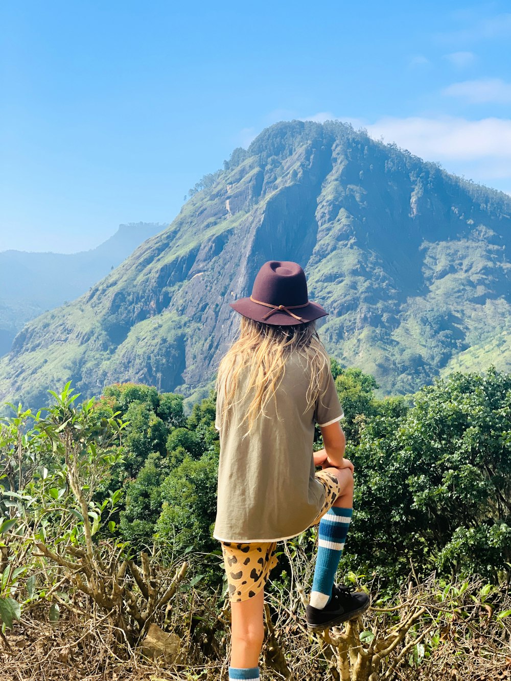 person wearing hat standing watching mountain during daytime