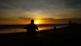 A peaceful sunset over the ocean with a silhouette of a girl sitting on the sand.