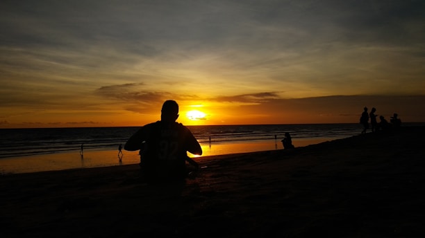 A vibrant sunset over a serene beach with a lone traveler sitting on the sand, soaking in the view.