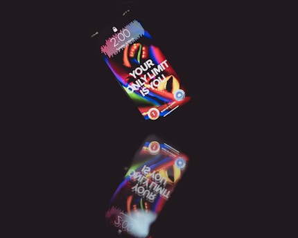 A smartphone displays a colorful, abstract wallpaper with the motivational text 'YOUR ONLY LIMIT IS YOU' on a dark background. The time shown on the screen is 2:00. The phone's reflection is visible below, creating an interesting visual effect.