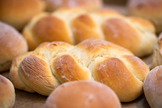 Freshly baked bread loaves with a golden brown crust, showcasing a variety of shapes including braided and round buns.