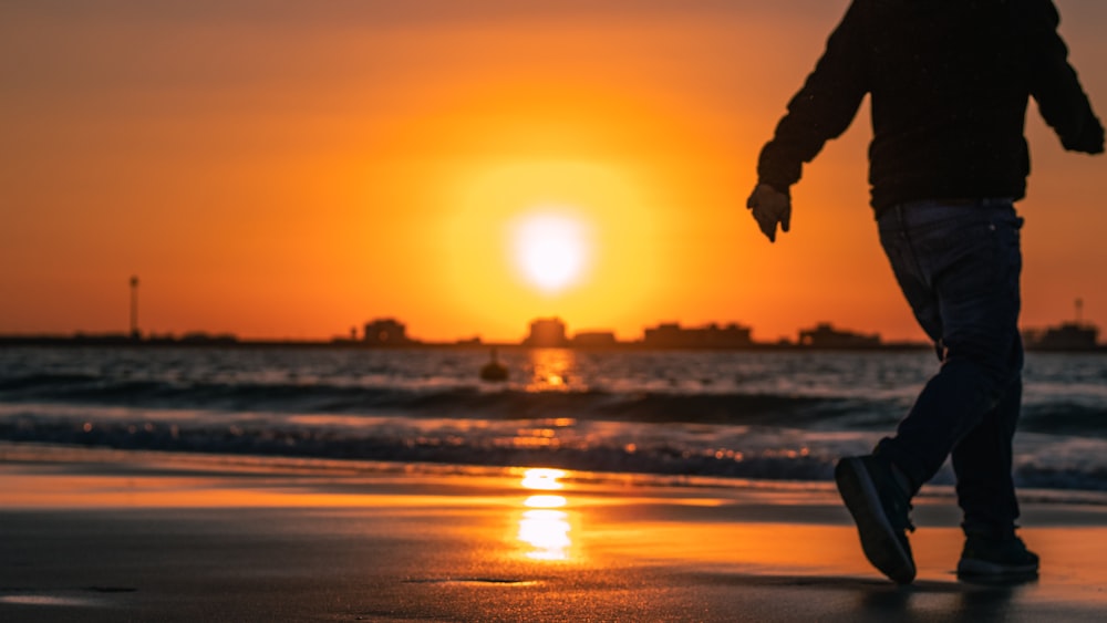 homem caminhando na praia durante o pôr do sol