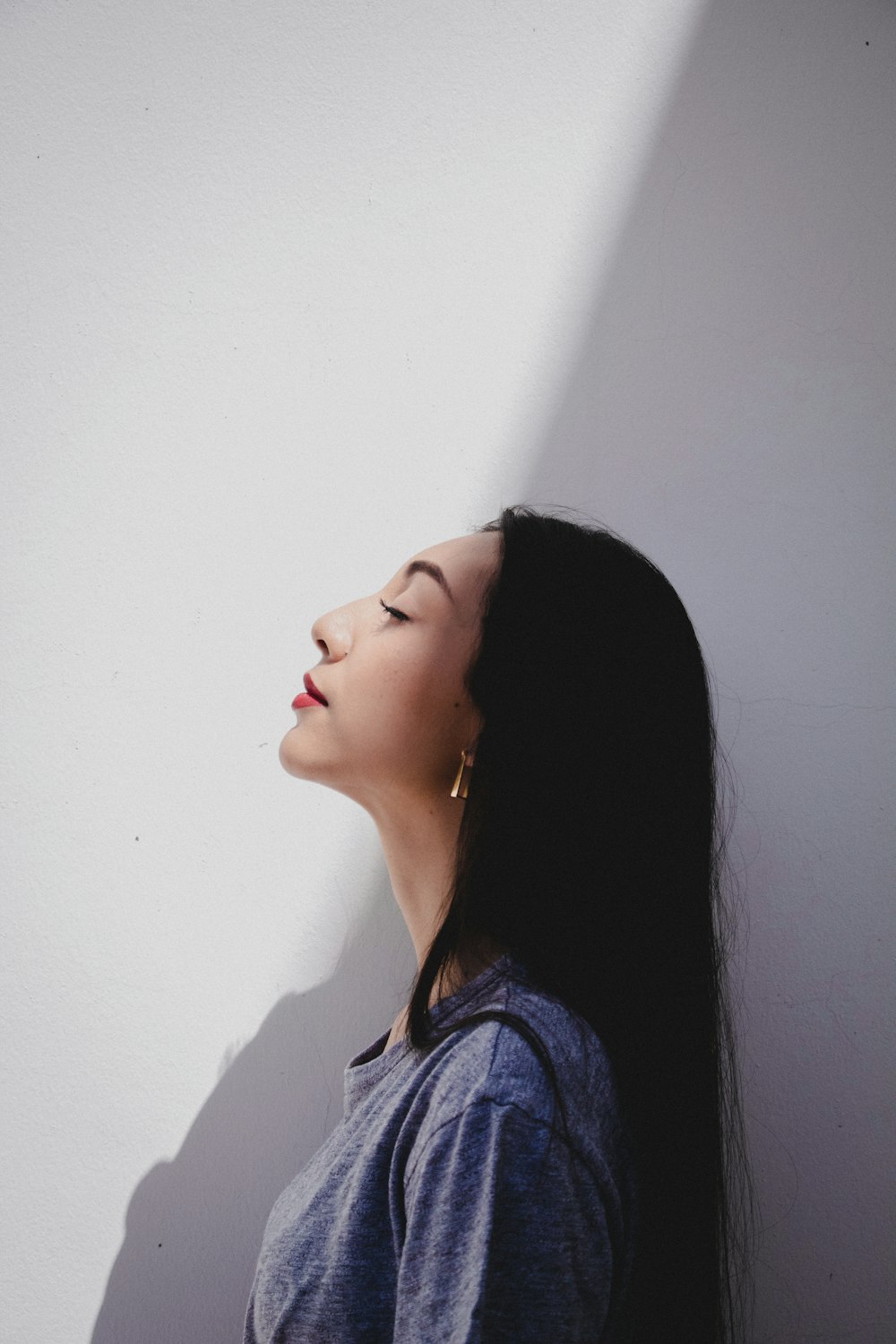 woman in grey shirt stands beside white painted wall