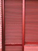 Red metal shutters with horizontal ridges are framed by red and pink brick walls.