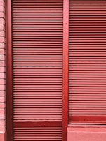 Red metal shutters with horizontal ridges are framed by red and pink brick walls.