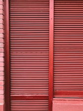 Red metal shutters with horizontal ridges are framed by red and pink brick walls.
