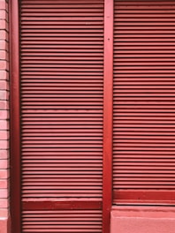 Red metal shutters with horizontal ridges are framed by red and pink brick walls.