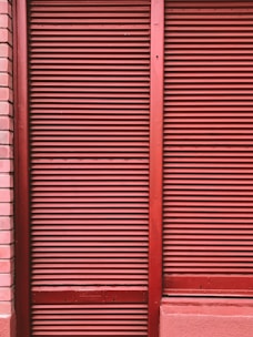 Red metal shutters with horizontal ridges are framed by red and pink brick walls.