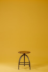 round brown wooden top and black base chair on yellow background