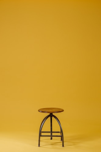 round brown wooden top and black base chair on yellow background